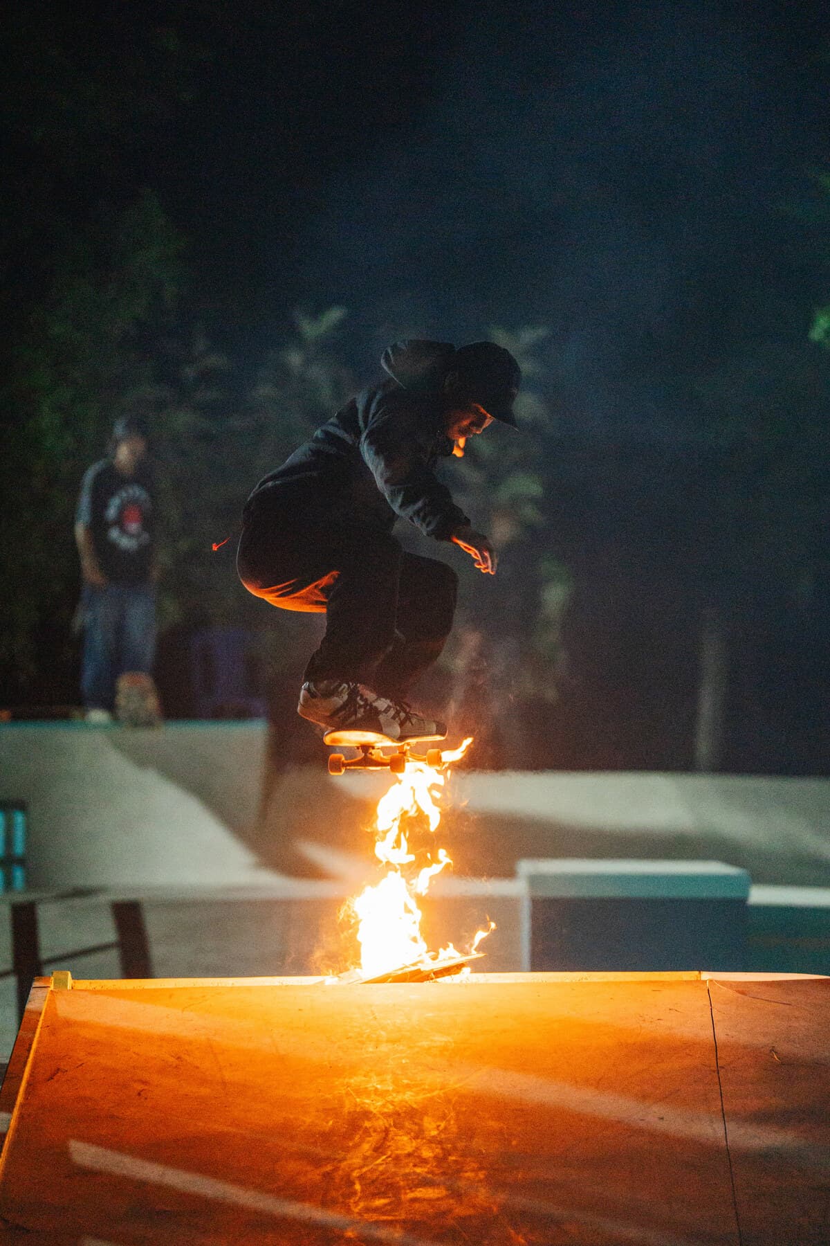 Skateboarder mid-air over a ramp lit by fire at night
