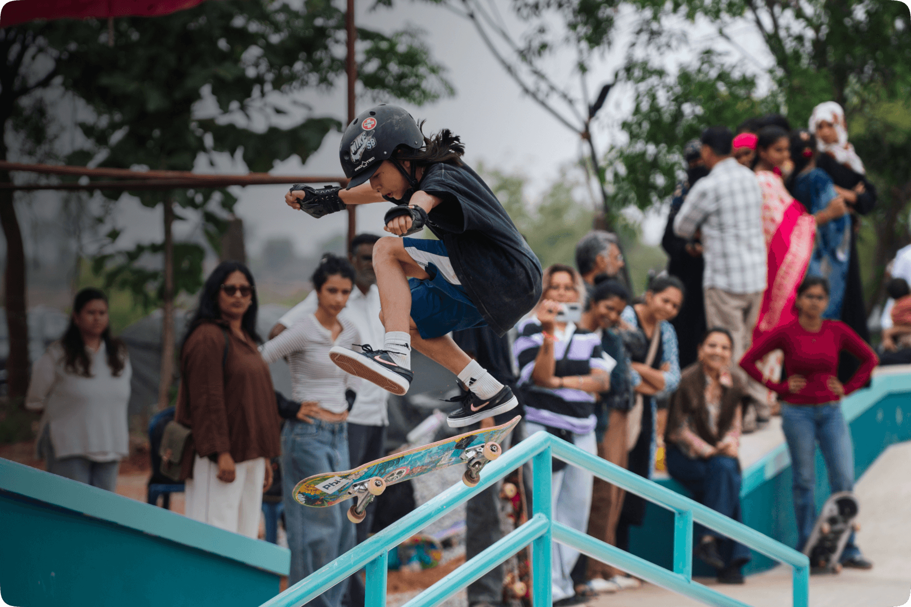 Student skateboarding over a rail in front of a crowd