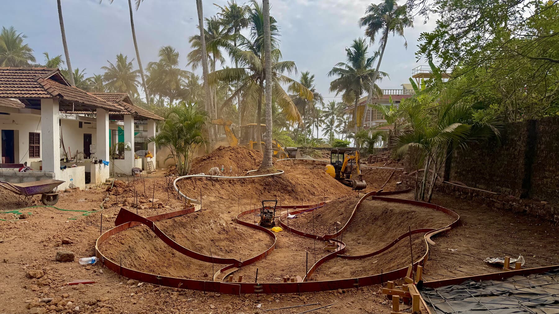 Skatepark under construction with steel formwork laid out among palm trees